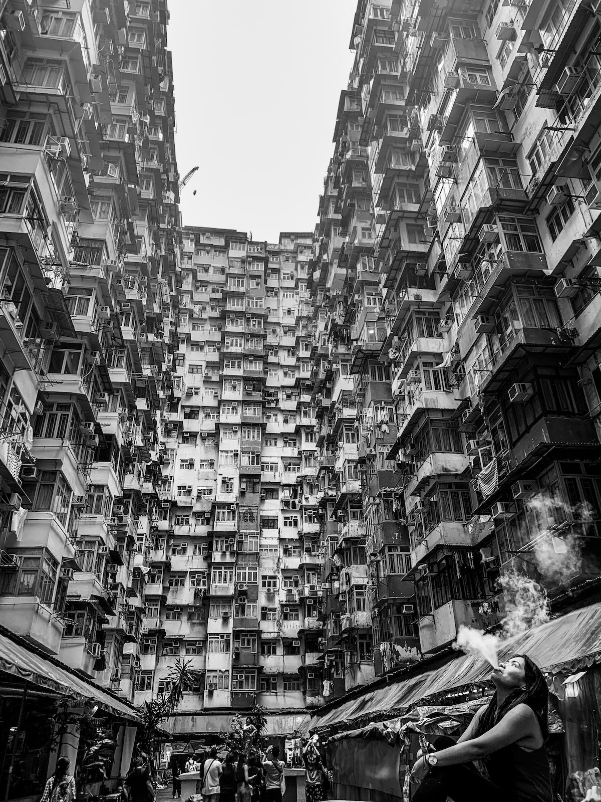The Ultimate Hong Kong Bucket List: 25 Best Things To Do! | monster building A lady blows smoke into the air below a busy set of flats, knowns as The Monster Building in Hong Kong.