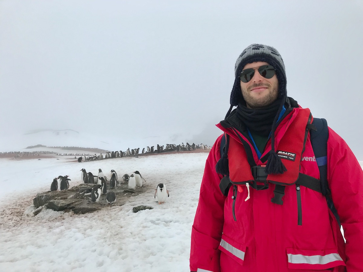 What To Expect on Your First Trip To Antarctica | penguins tourist Antarctica A male tourist in a red parks stands next to a waddle of penguins