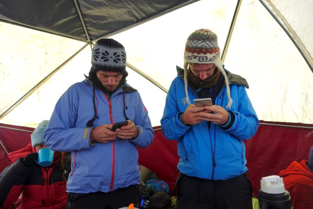 The Only Road Trip Packing List You'll Ever Need! | technology while camping Two men in cold weather clothing check their phones intensely