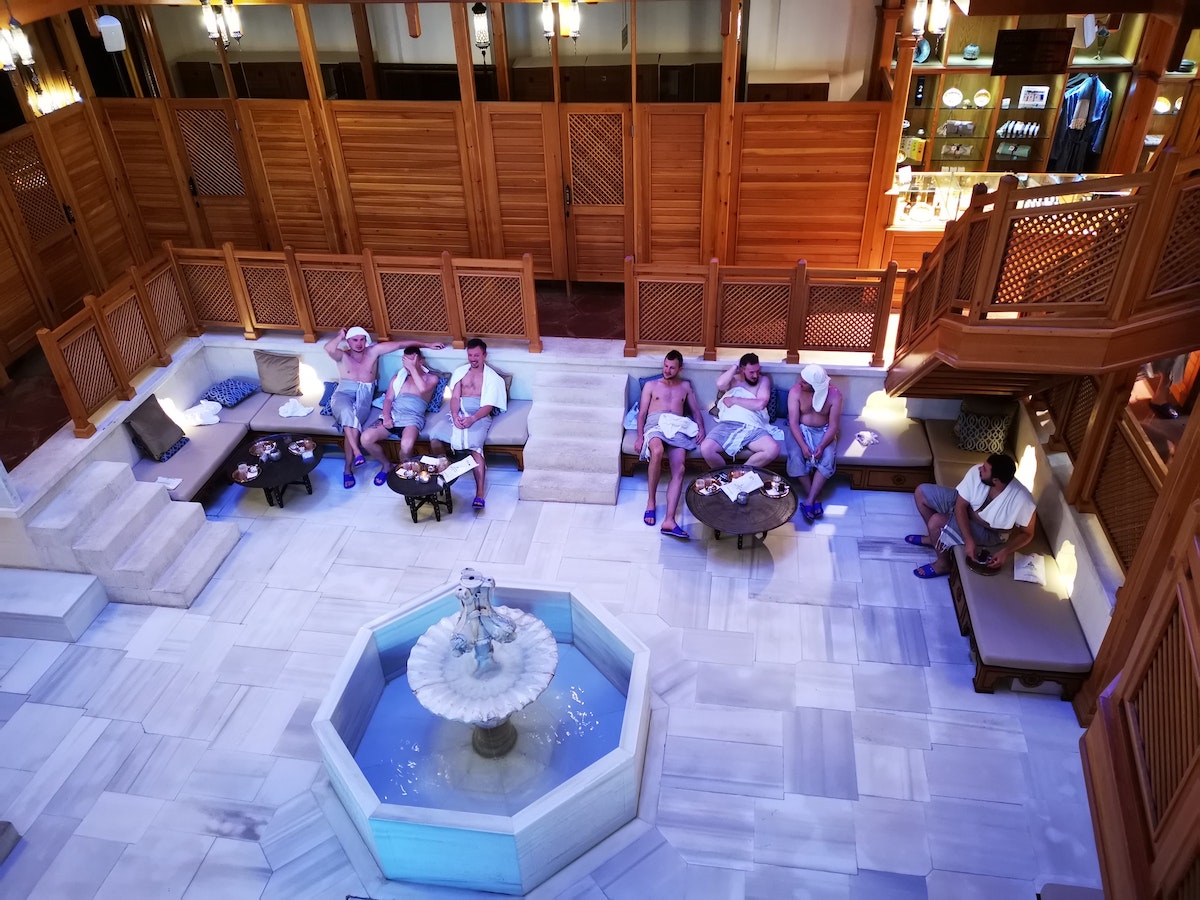 Turkish Bath For Men: My (Honest) First-Timer’s Experience! | turkish bath males Men sit and talk with each other with towels around their waists in a Turkish hammam.